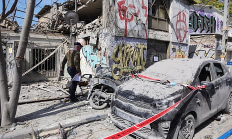 A man walks past a destroyed building and car that are covered in dust and ash