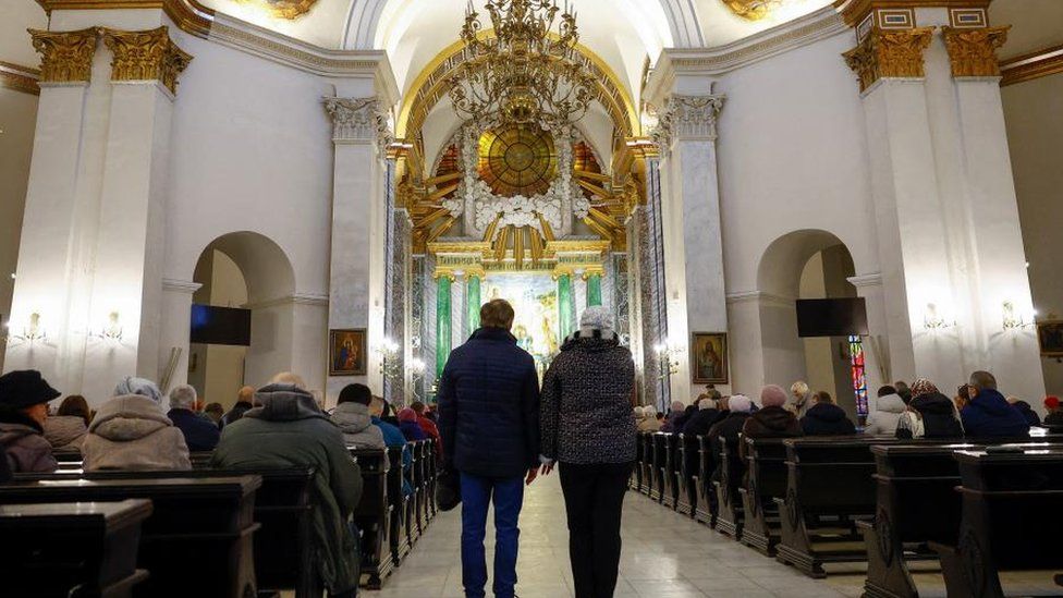 Besimtarja katolike Lesia Shestakova dhe besimtari ortodoks Oleksandr Shestakov, të cilët përgatiten për të festuar Krishtlindjet së bashku në të njëjtën ditë për herë të parë, qëndrojnë brenda Katedrales së Shën Aleksandrit përpara një shërbese.